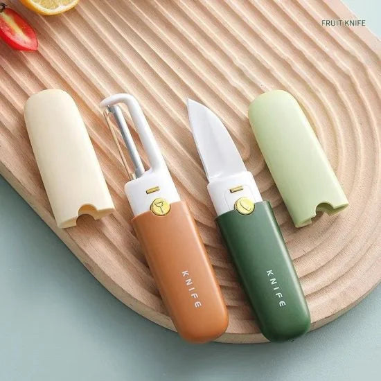 Two compact 2-in-1 fruit knife and peeler tools, one orange and one green, displayed with their matching protective covers on a grooved wooden board.