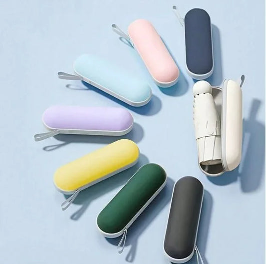 Eight colorful pill-shaped capsule umbrella cases arranged in a circle on a light blue background, with the white case opened to reveal a folded mini umbrella inside.