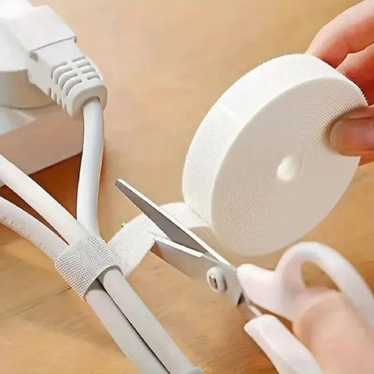 A person using scissors to cut a strip from a roll of white Velcro tape to wrap and organize electrical cables.