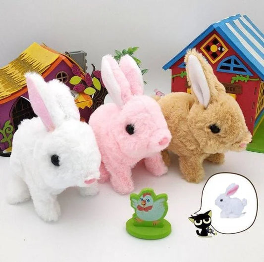 Three fluffy interactive walking and talking plush rabbit toys in white, pink, and light brown, displayed alongside colorful toy houses and a small green chicken figure.