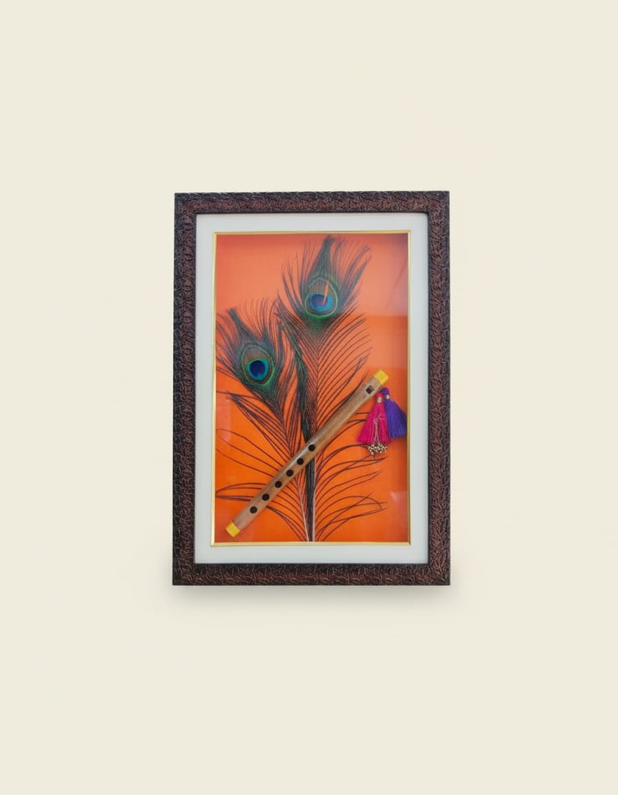 A framed shadow box wall art featuring a traditional wooden flute with colorful tassels crossed over two vibrant peacock feathers, all set against a bright orange background.