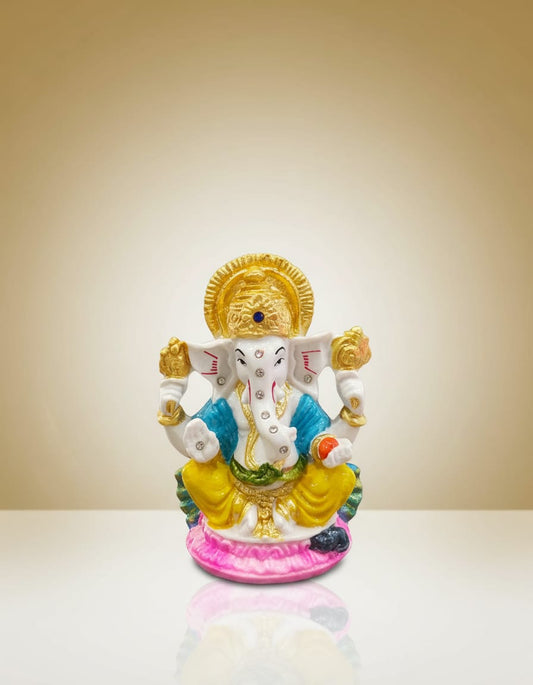 A beautifully detailed Lord Ganesha idol featuring a white body, golden crown, blue and yellow garments, seated peacefully on a bright pink lotus base.