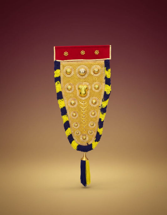 A traditional Kerala Nettipattam wall hanging featuring an intricate golden centerpiece bordered by a red band at the top and black and yellow fringed edges, finishing with a bottom tassel.