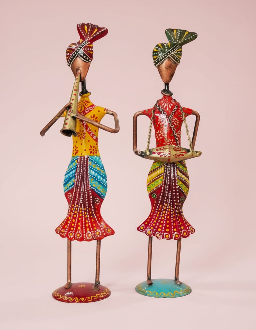 A set of two colorful handpainted metal figurines depicting traditional Rajasthani musicians, one playing a wind instrument and the other holding a drum, displayed against a light pink background.