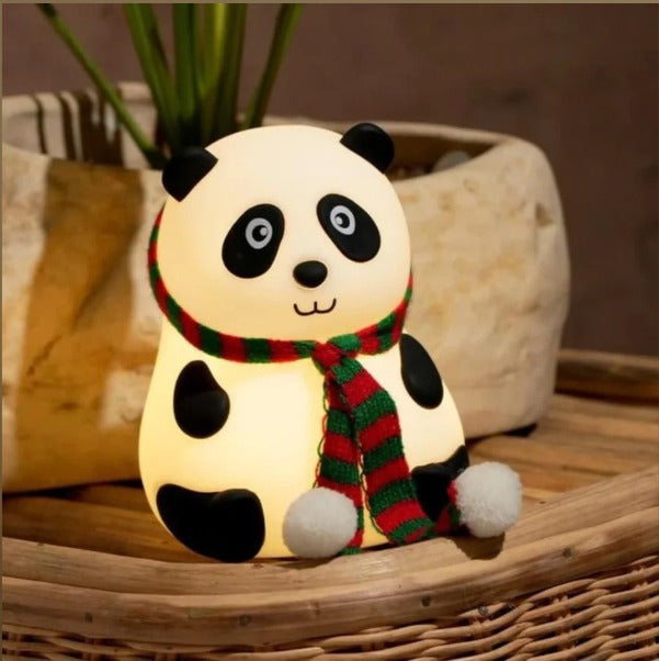 A cute, glowing panda-shaped LED night lamp wearing a red and green striped scarf with white pom-poms, resting on a woven rattan surface.